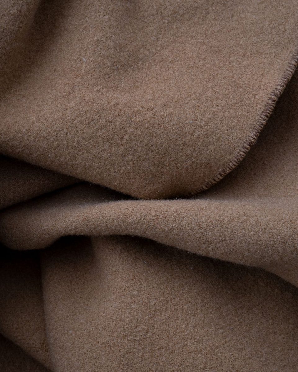 A folded wool throw on the corner of a bed